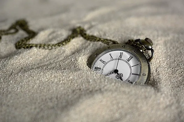pocket watch that can help with time optimisation lying half buried in white sand